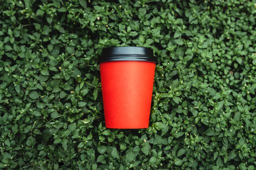 A Red paper cup coffee resting on a green floral background
