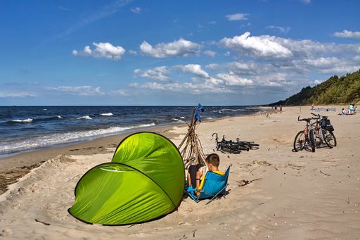 Tourist reading a book sitting in beach chair by the green tent on a sea beach.