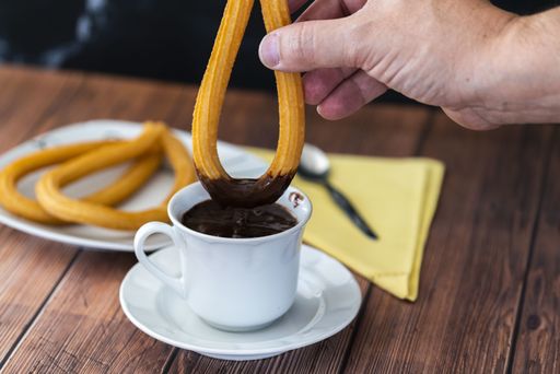 A hand dipping churros in hot chocolate