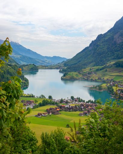A vertical shot of a small village by a lake surrounded by mountains
