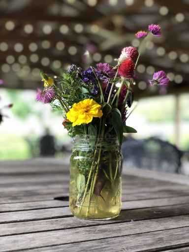 A close up of a flower bouquet in a glass jar filled with water on a wooden table