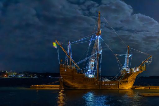 A sailing ship in port at night under a moonlit sky