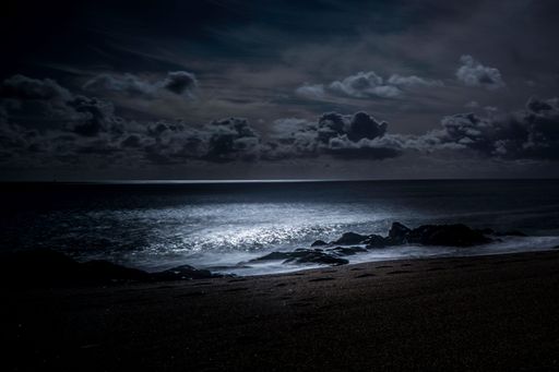 A scenic view of a pebbled beach with footprints against sea waves illuminated by moonlight