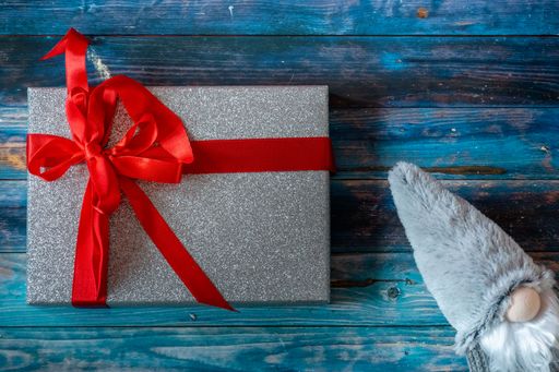 A top view of a cute Christmas gnome toy and a present on a blue wooden surface with copy space