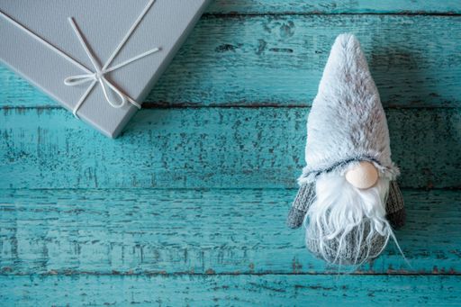 A top view of a cute Christmas gnome toy and a present on a blue wooden surface with copy space
