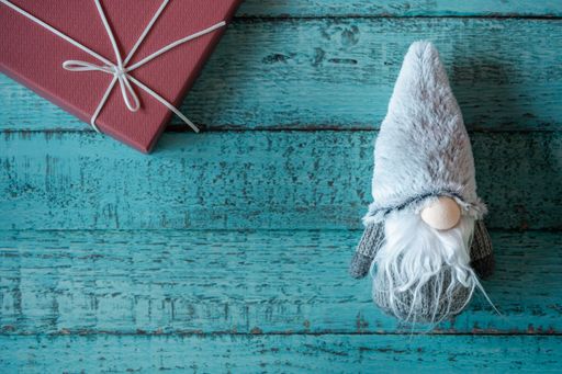 A top view of a cute Christmas gnome toy and a present on a blue wooden surface with copy space