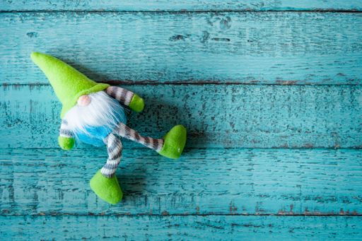 A top view of a cute green Christmas gnome toy on a blue wooden surface with copy space