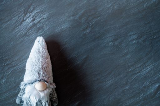 A top view of the gnome with a long, white beard and round nose in a gray hat on a dark surface - the concept of New Year