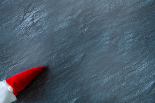 A top view of the Santa Claus toy with a long, white beard in a red hat on a dark surface - the concept of New Year