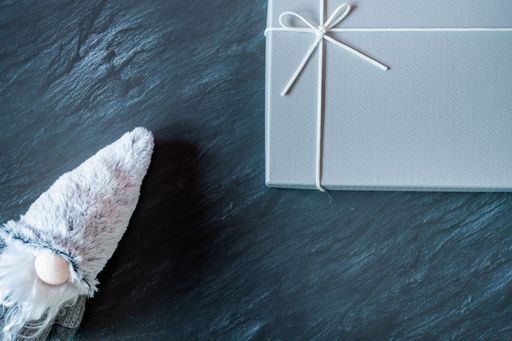 A top view of a winter gnome plush toy and a gray gift box on a dark marble table