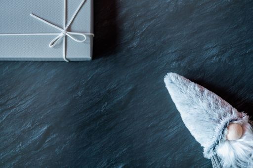 A top view of a winter gnome plush toy and a gray gift box on a dark marble table