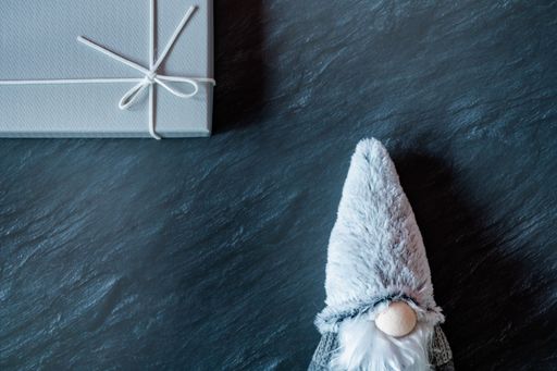 A top view of a winter gnome plush toy and a gray gift box on a dark marble table