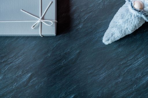 A top view of a winter gnome plush toy and a gray gift box on a dark marble table