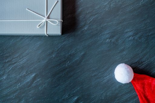 A top view of a winter gnome plush toy and a gray gift box on a dark marble table