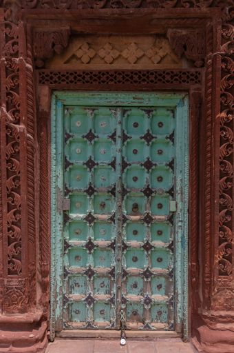 A vertical shot of an old green door in Indian-style decorations