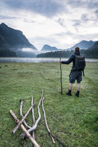 A hiker with a backpack enjoying a beautiful view of the lake and mountains on a cloudy day