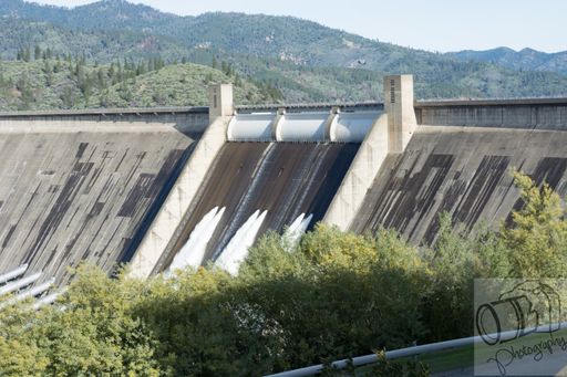 A picture of Shasta Dam surrounded by greenery and mountains under a blue sky during daytime