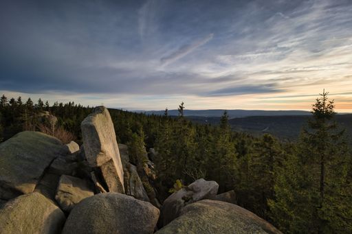 A scenic view of landscape with forested hills under cloudy sunset sky