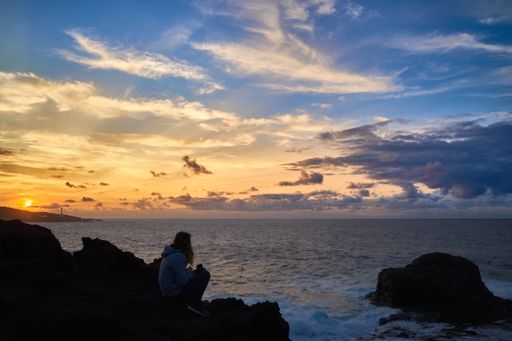 A woman sitting on a rocky coast enjoying the beautiful sunset in Gran Canaria, Canary Island