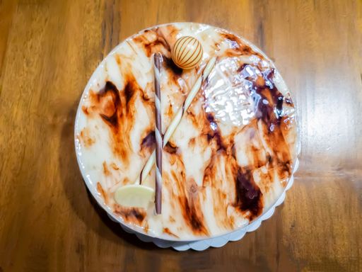 top view of a delicious white chocolate cake decorated with a chocolate ball and elongated wafers and a chocolate candy bar, on a wooden table