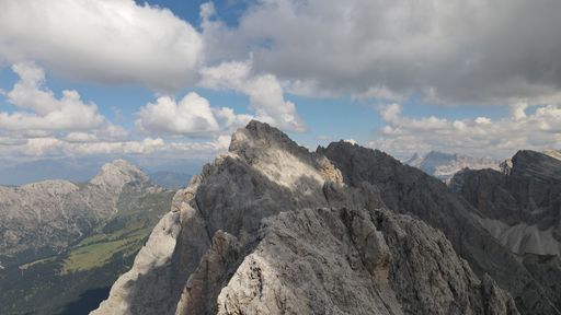 An aerial shot of the Seceda Mountain peak with floating clouds above in the Alps of Italy