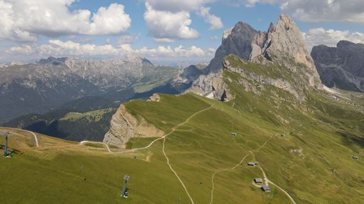 An aerial shot of Seceda Mountain and a vast valley with floating clouds above in the Alps of Italy