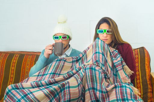 A closeup shot of a couple covered in a blanket wearing 3D glasses for watching a movie
