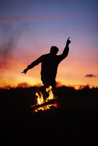 A silhouette of a person dancing with a blurry background and a campfire during a beautiful sunset