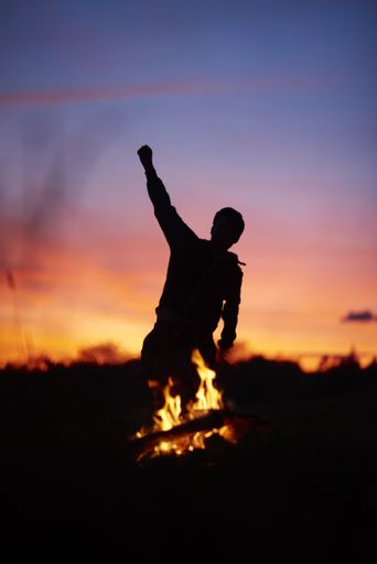 A silhouette of a person dancing with a blurry background and a campfire during a beautiful sunset