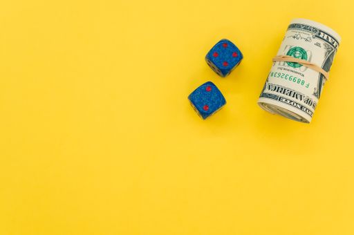 A bundle of rolled-up American banknotes and two dice isolated on a yellow background