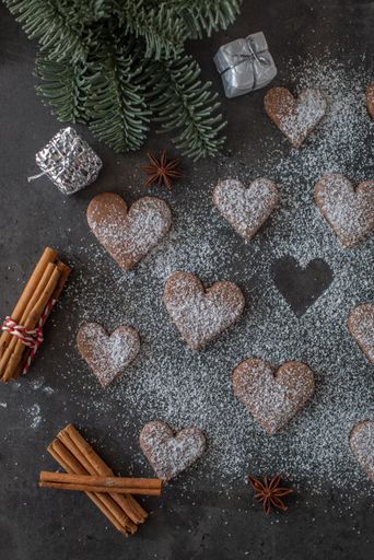 A vertical top view of gingerbread heart-shaped cookies with sugar powder