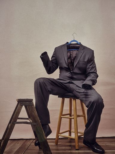 A vertical shot of a male suit sitting on a chair like a male