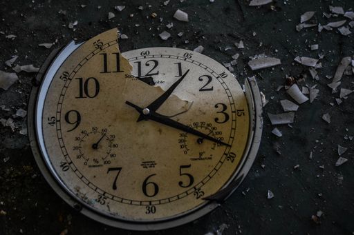 A closeup shot of a broken clock with the shards flown apart on the ground