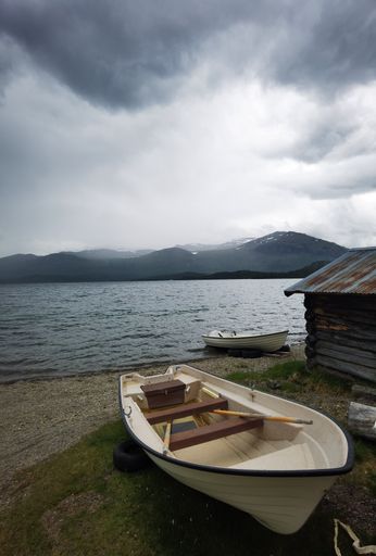 A vertical shot of a boat on the shore of a sea with mountains and a cloudy sky in the background