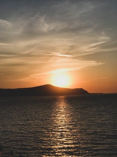 A vertical shot of the sea surrounded by hills under the sunlight during the sunset