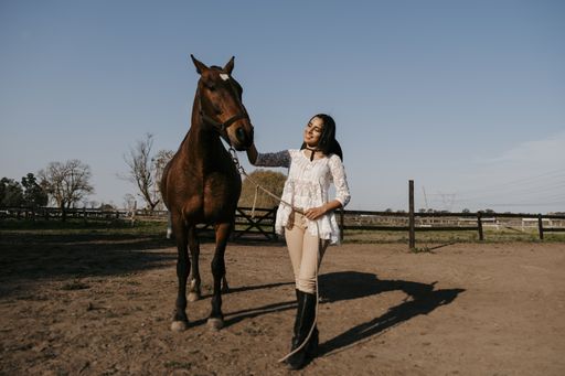 A vertical shot of a young Latina female posing with her brown horse