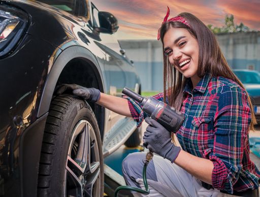 a white female car mechanic working on the tire in a squat position
