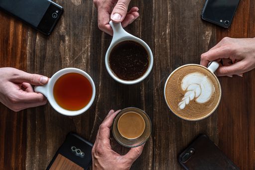 A high angle shot of four phones on the table and people holding cups with different types of coffees