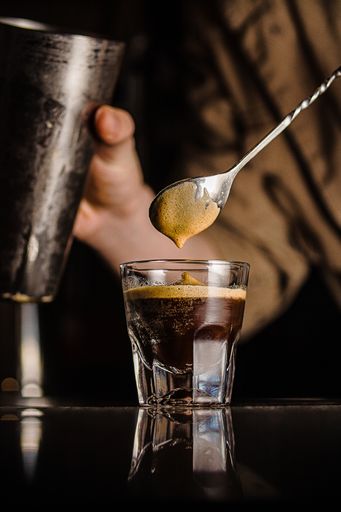 A vertical closeup shot of a person stirring the coffee in a small glass