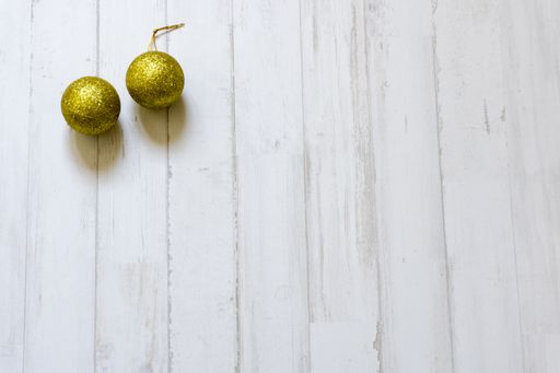 Two golden glitter Christmas tree balls on a white wooden background with a copy space