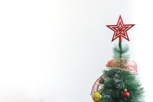A little Christmas tree with a red star on top decorated with red and gold balls and decorative ribbon with copy space