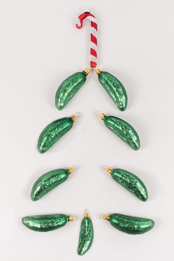 Christmas tree baubles in the shape of a cucumber are lying on a white background. They are arranged like a Christmas tree and a candy cane is on top.