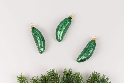 Three Christmas tree baubles in the shape of a cucumber are lying on a white background. Fir branches decorate the picture.