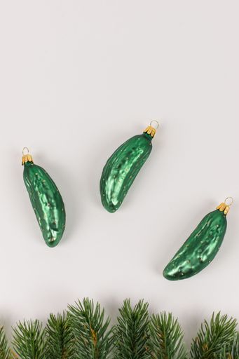 Three Christmas tree baubles in the shape of a cucumber are lying on a white background. Fir branches decorate the picture.