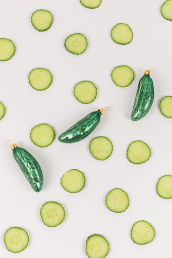 Three Christmas tree baubles in the shape of a cucumber are lying on a white background. Cucumber slices decorate the picture.