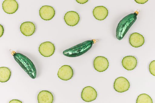 Three Christmas tree baubles in the shape of a cucumber are lying on a white background. Cucumber slices decorate the picture.