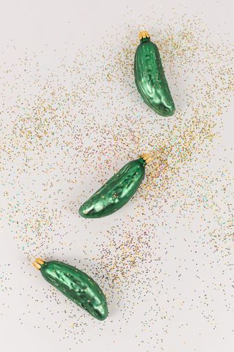 Three Christmas tree baubles in the shape of a cucumber are lying on a white background. Glitter decorate the picture.