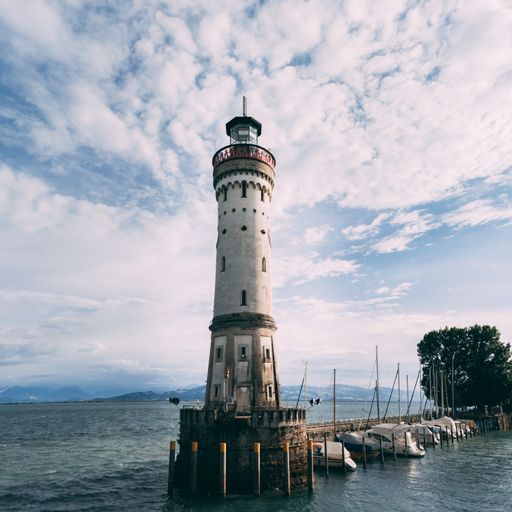 A low angle shot of ships near a white lighthouse in the sea under the beautiful cloudy sky