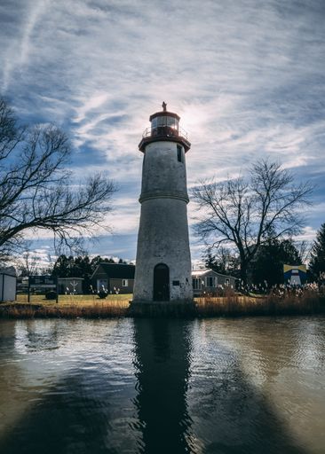 A vertical low angle shot of a white concrete lighthouse reflecting in the lake under the cloudy sky
