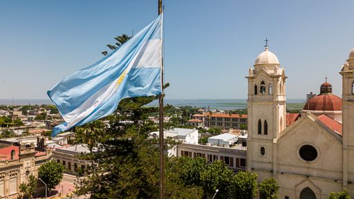A closeup of Argentinian flag waving in the wind against a blue sky with Victoria city in the background, Entre Rios, Argentina